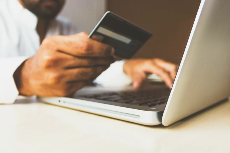 Person shopping online with a laptop and a bank card in hand